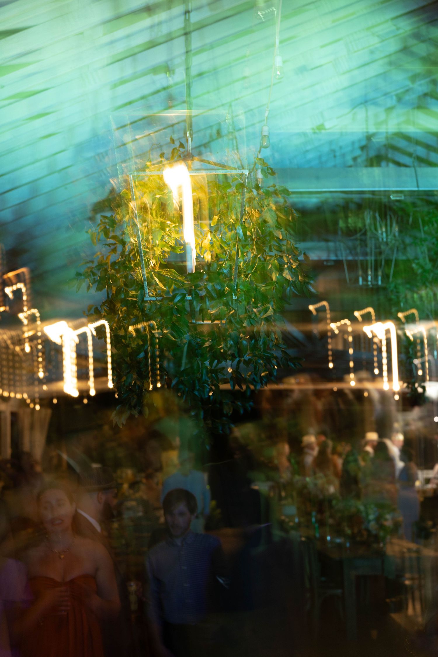 Long exposure abstract shot of wedding reception with hanging floral lantern and dancing guests.