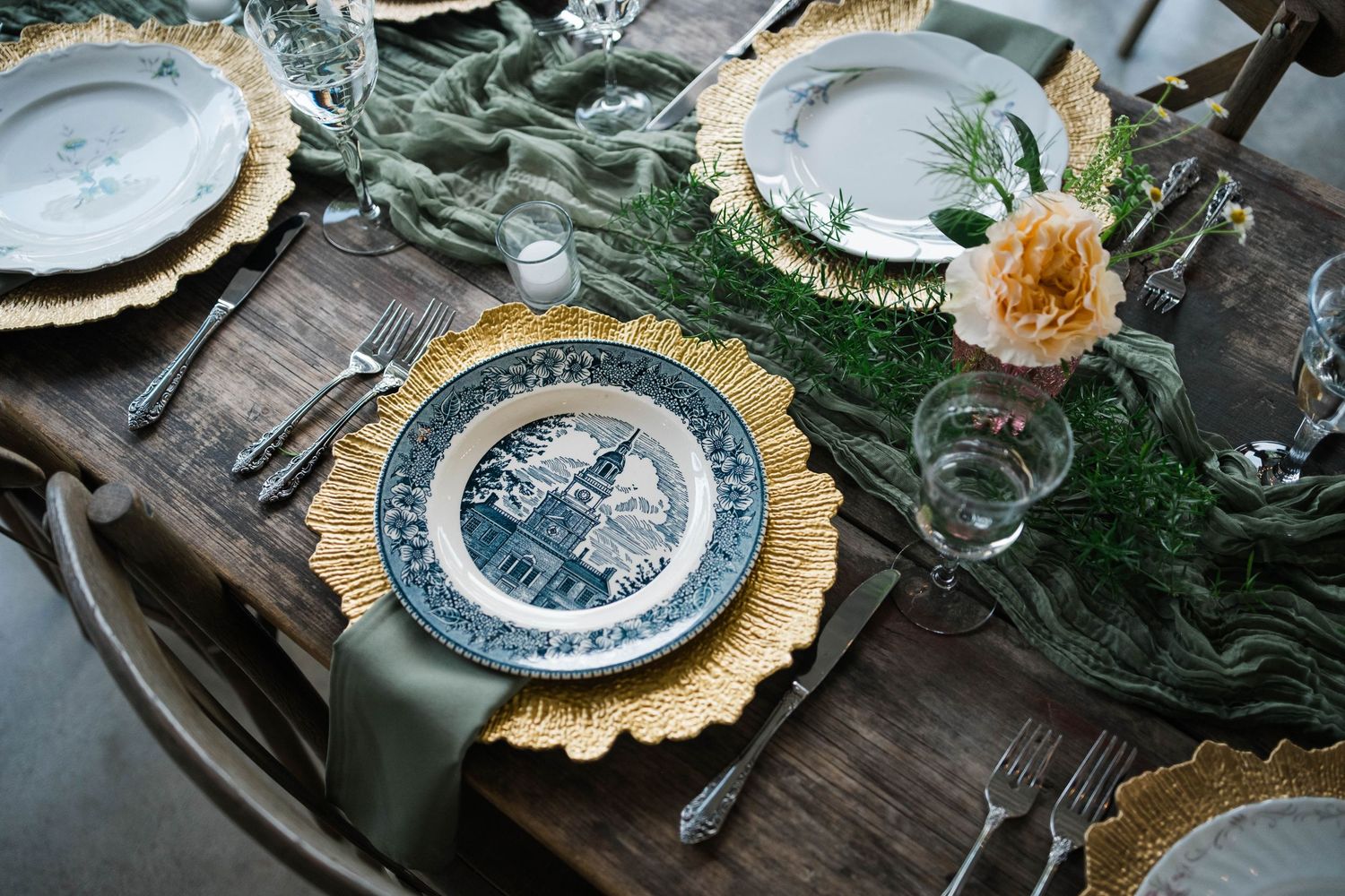 Elegant wedding table setting with gold chargers, blue floral plates, and green velvet runner.