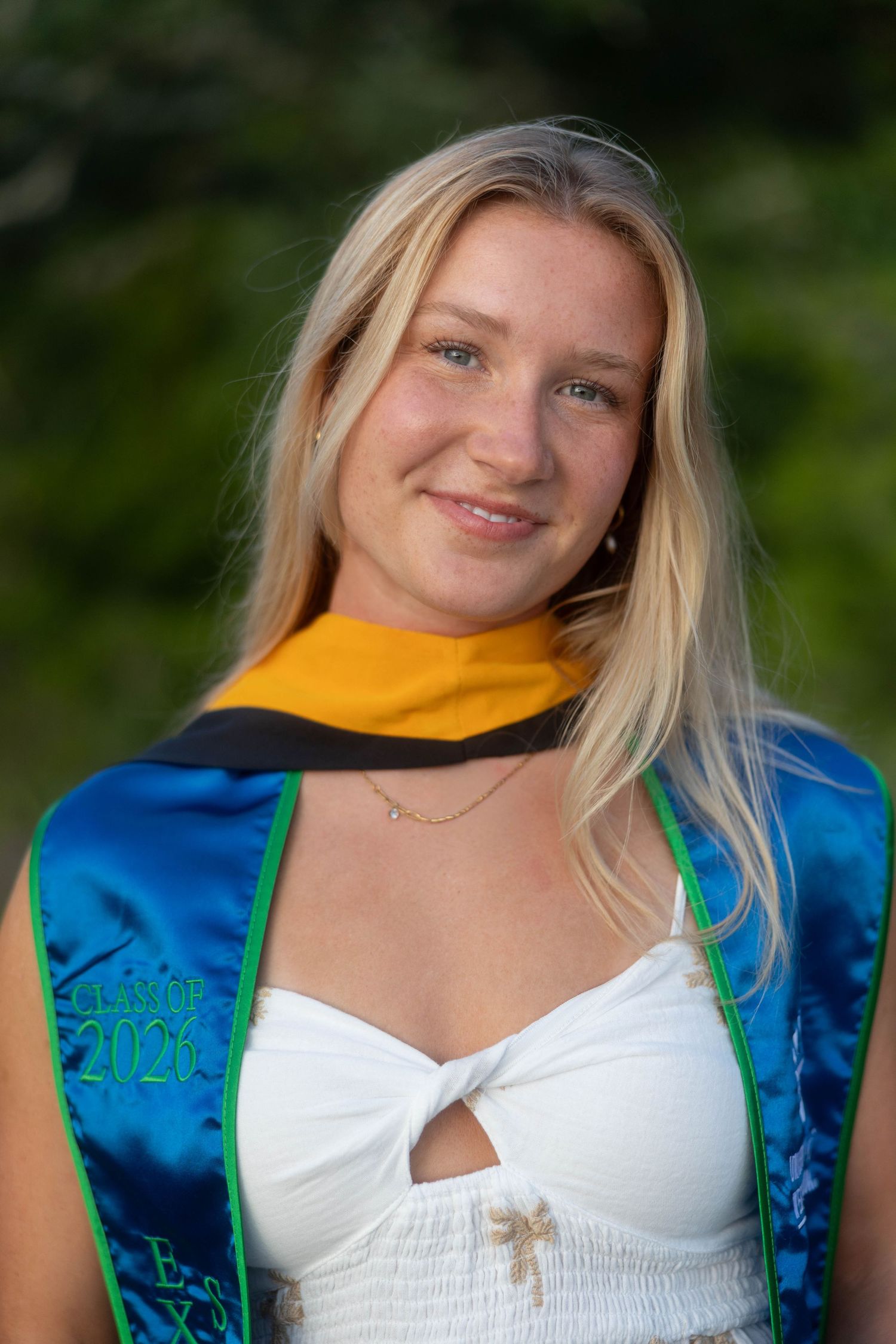 Smiling blonde woman wearing Class of 2026 graduation sash outdoors in natural light.

College and high school graduation photographer