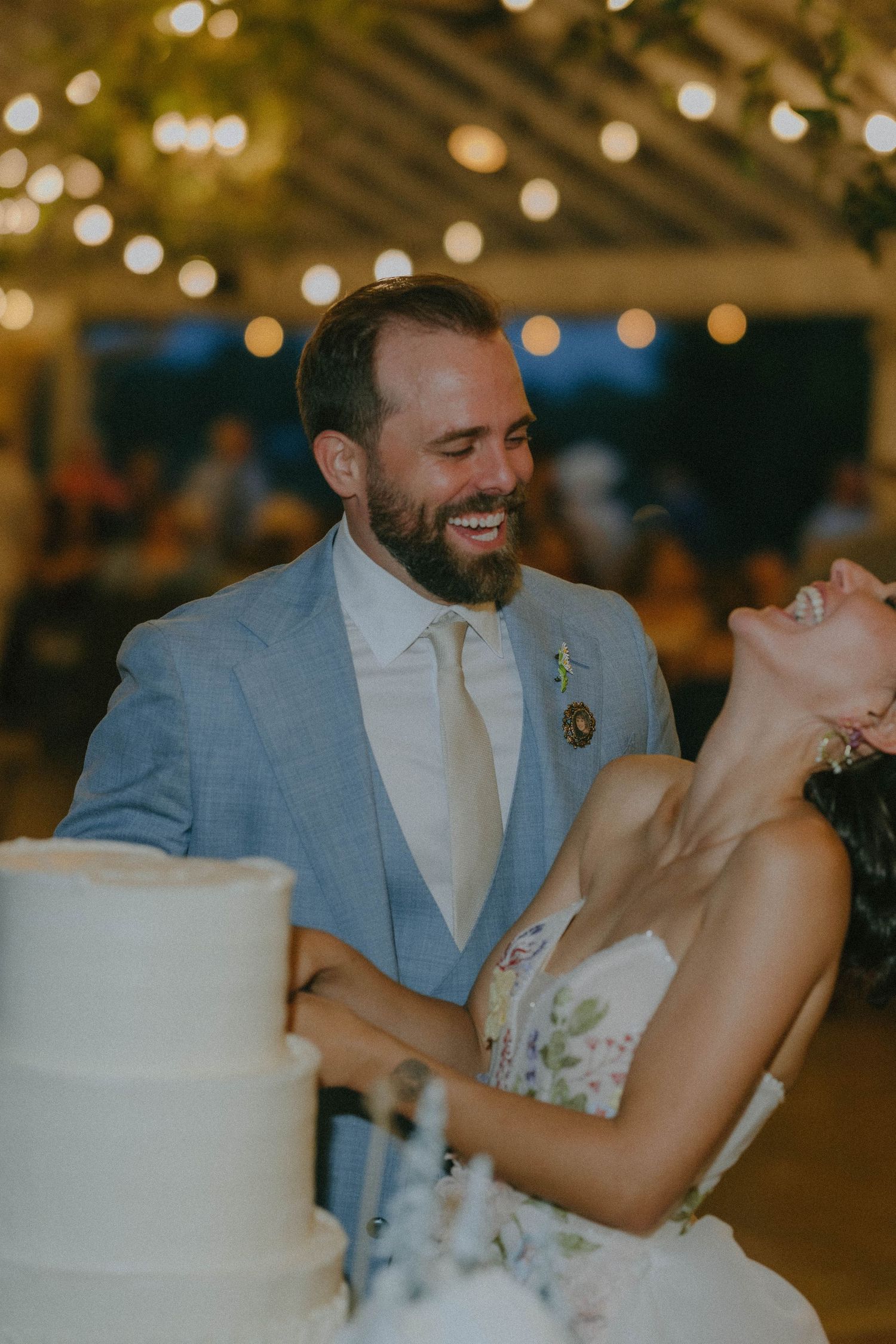 Laughing bride and groom sharing a joyful moment while cutting their tiered wedding cake.