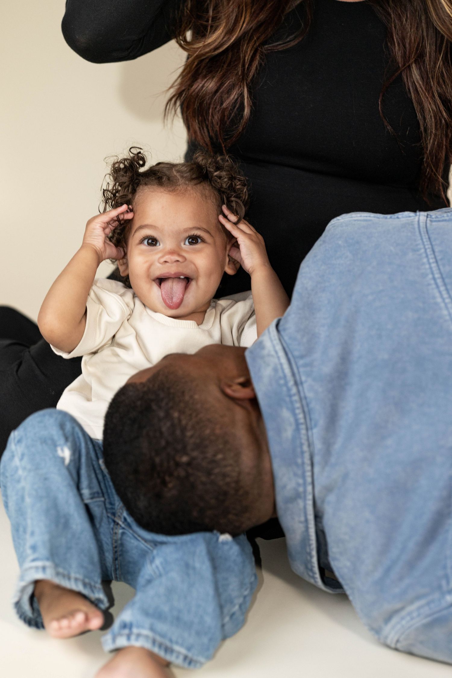Playful toddler sticking tongue out while sitting between parents during family maternity photo session.