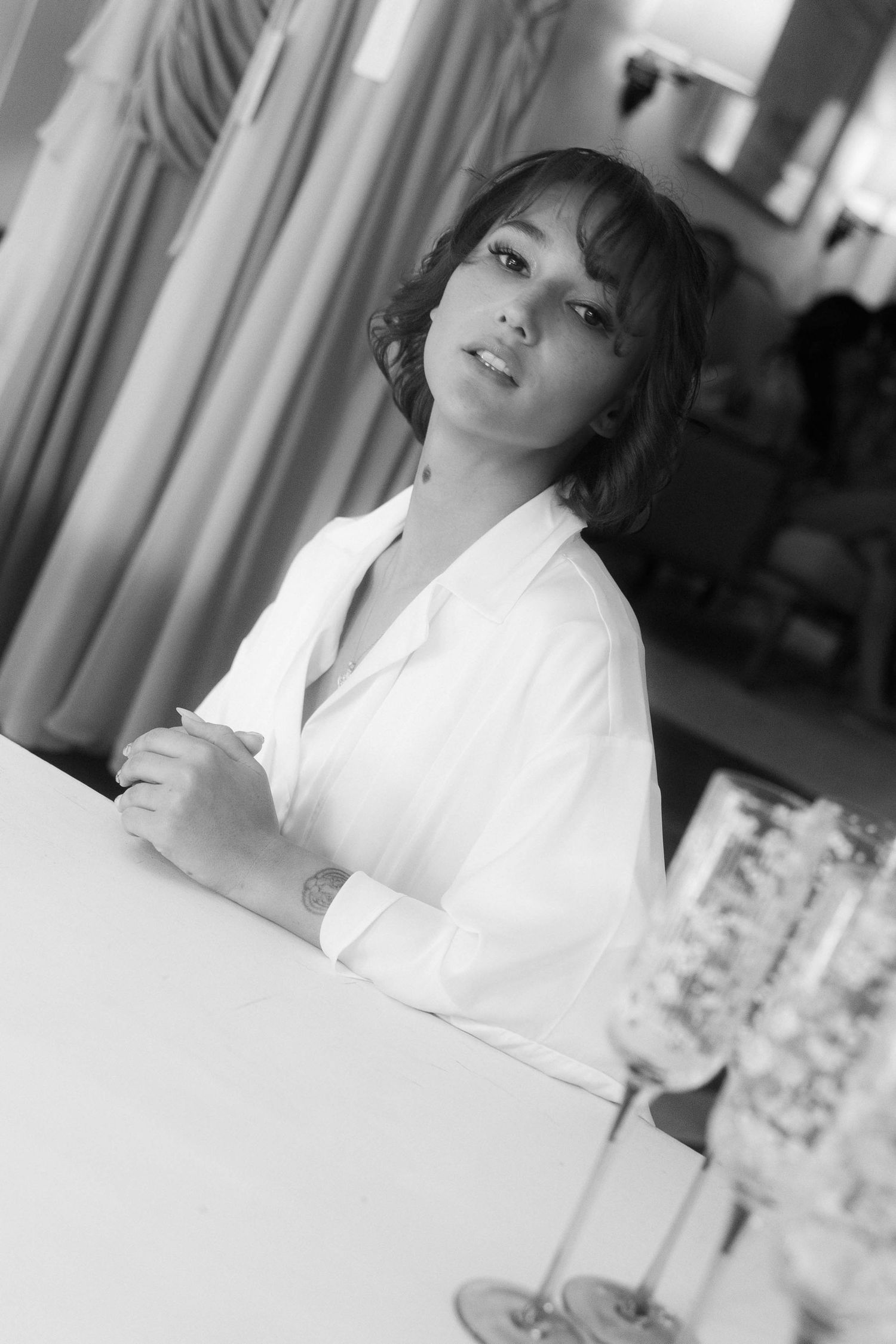 Black and white portrait of woman in white shirt seated at table indoors.