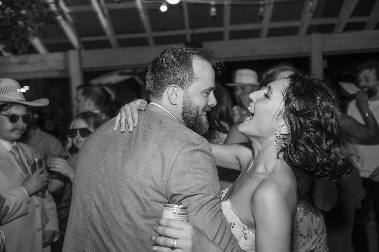 Bride and groom share a joyful laugh while dancing together at their wedding reception in black and white.