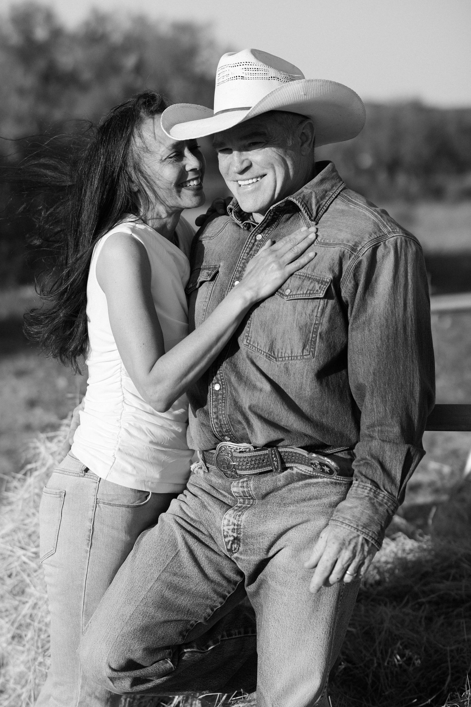Black and white photo of smiling cowboy couple in jeans and denim shirt with white cowboy hat.