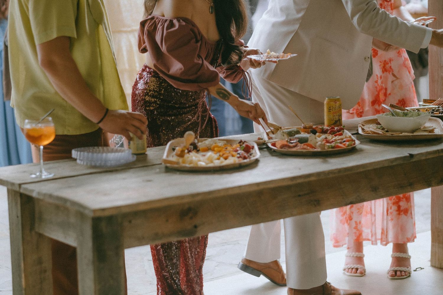 Wedding guests gather around a rustic wooden table enjoying appetizers and charcuterie during cocktail hour.