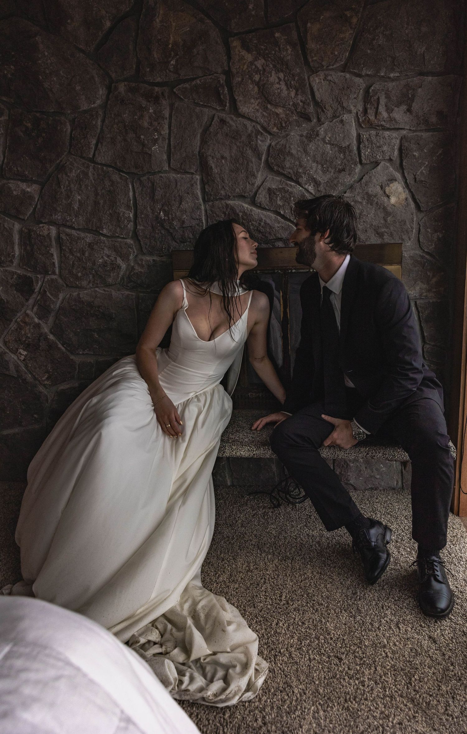 A sequence of romantic wedding photos showing a couple sitting together against a stone wall in dim lighting.