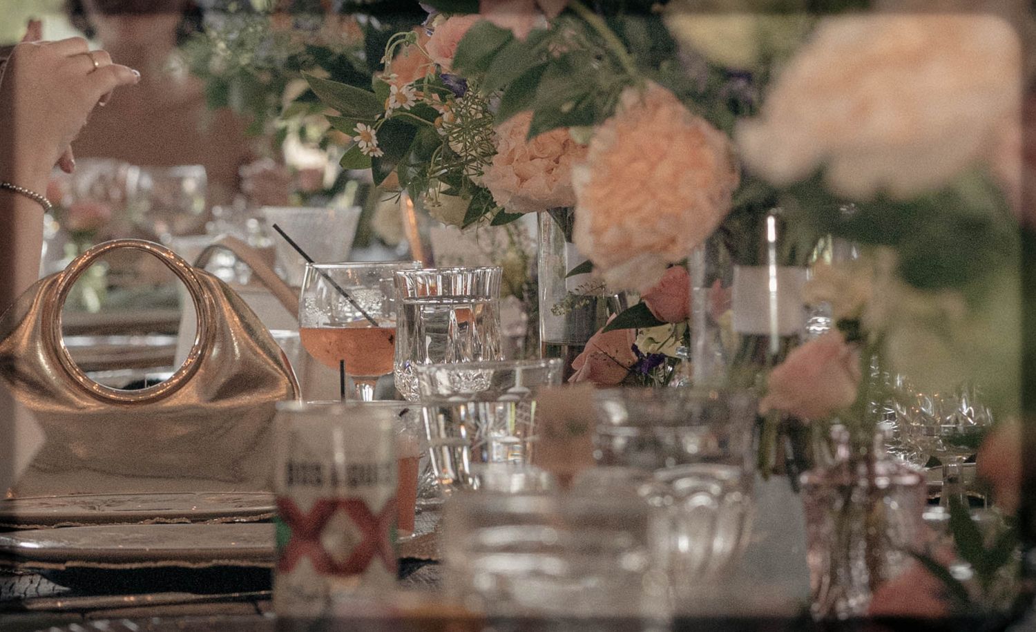 Elegant wedding table setting with crystal glassware, pink floral centerpieces, candles, and gold napkin rings.