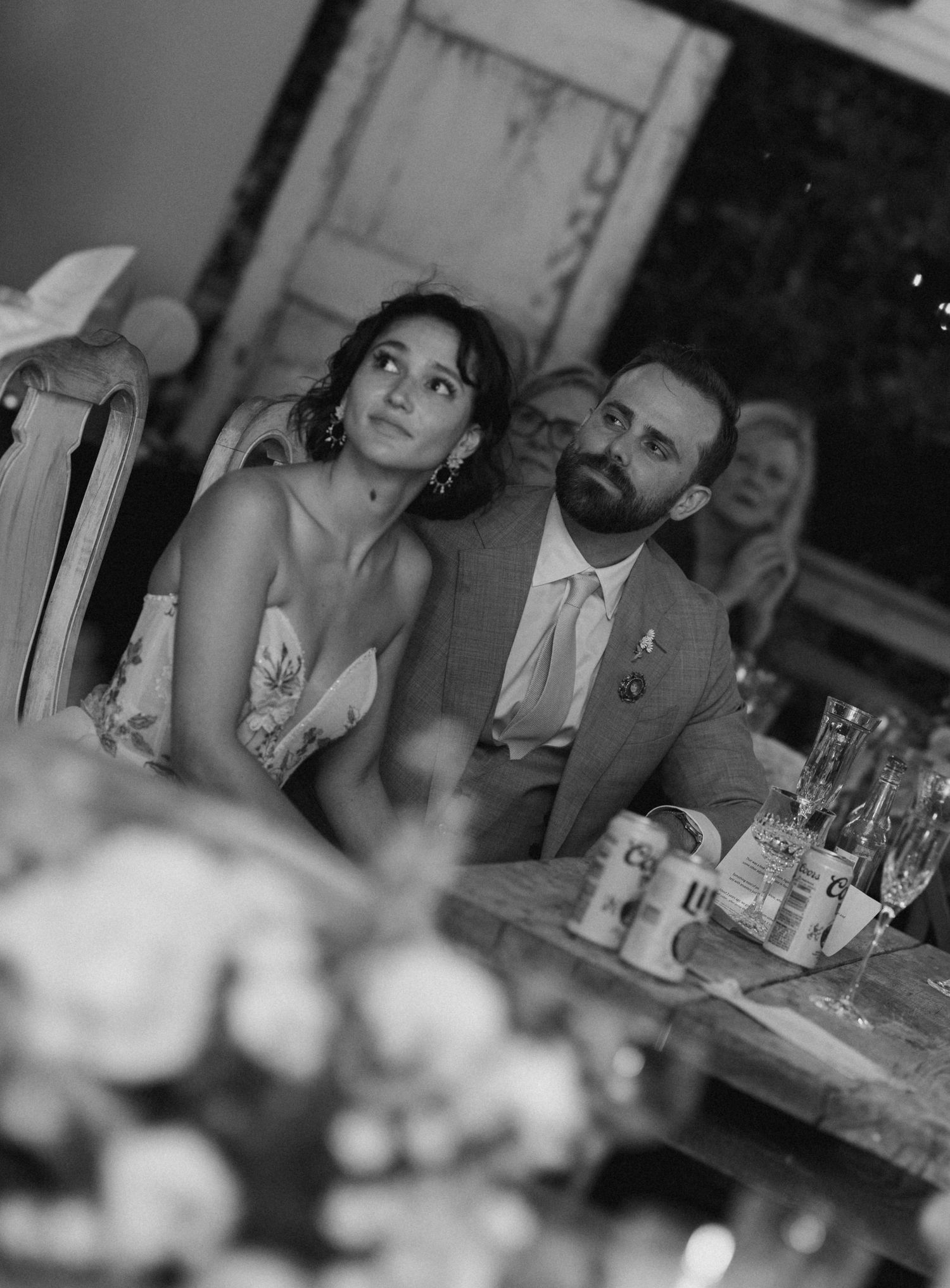 Black and white photo of bride and groom listening to toasts at their wedding reception.