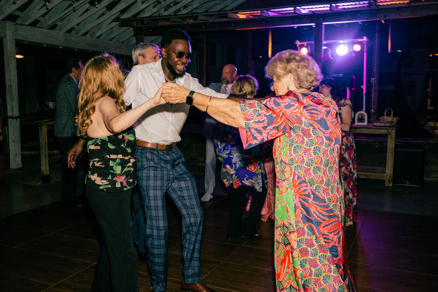 Guests of all ages dance together energetically on the wooden dance floor at a lively wedding reception.