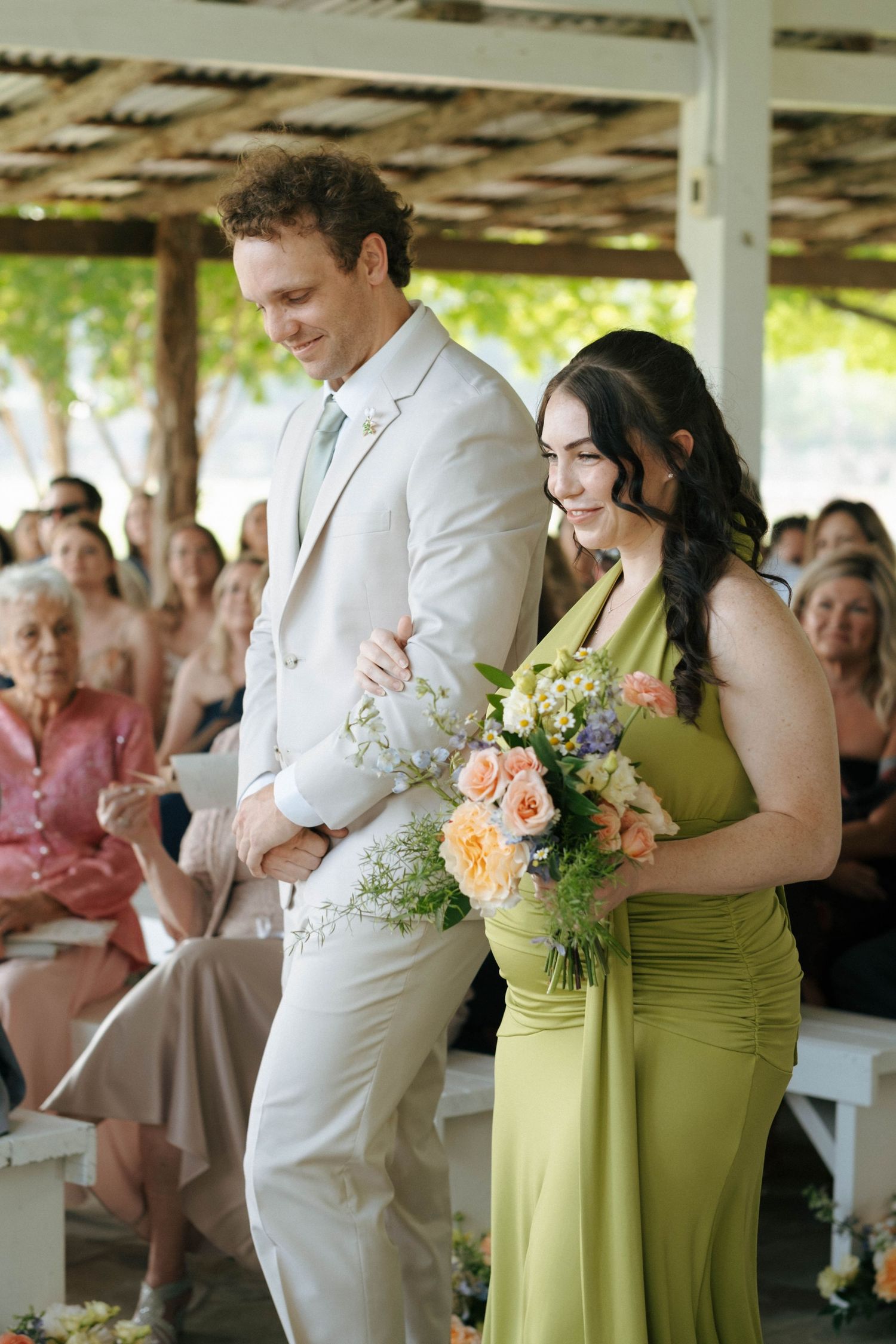 Groomsman in white suit escorts bridesmaid in green dress down wedding aisle.