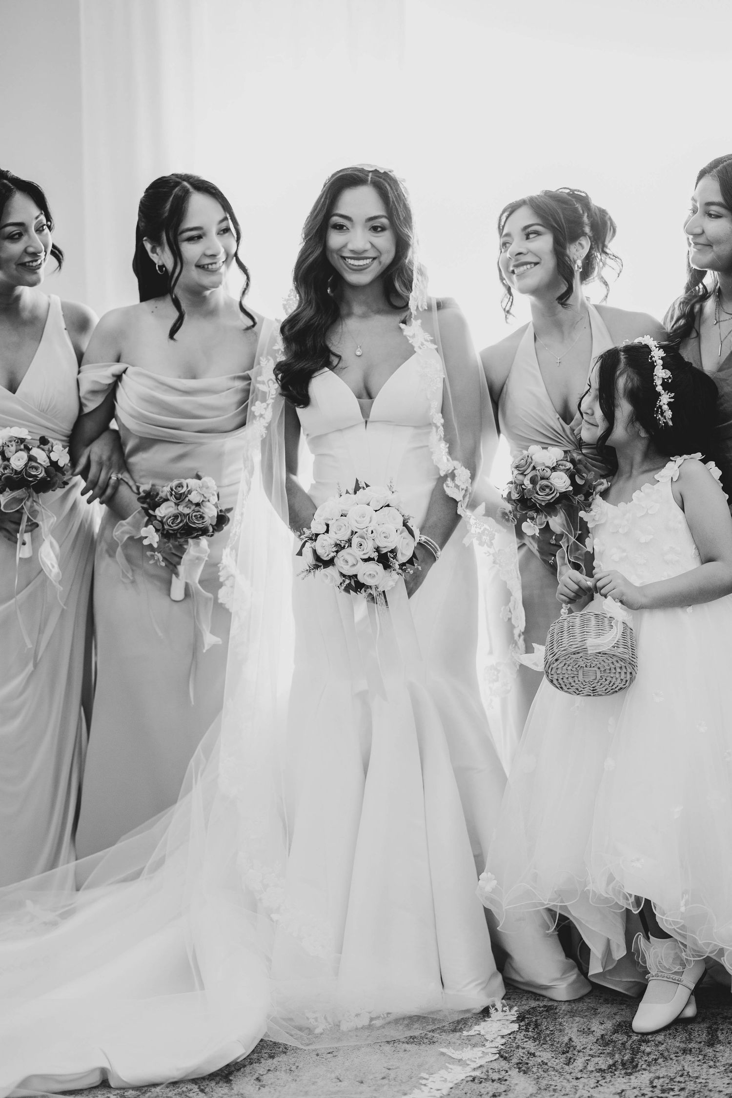 Black and white photo of radiant bride posing with bridesmaids and flower girl holding bouquets.