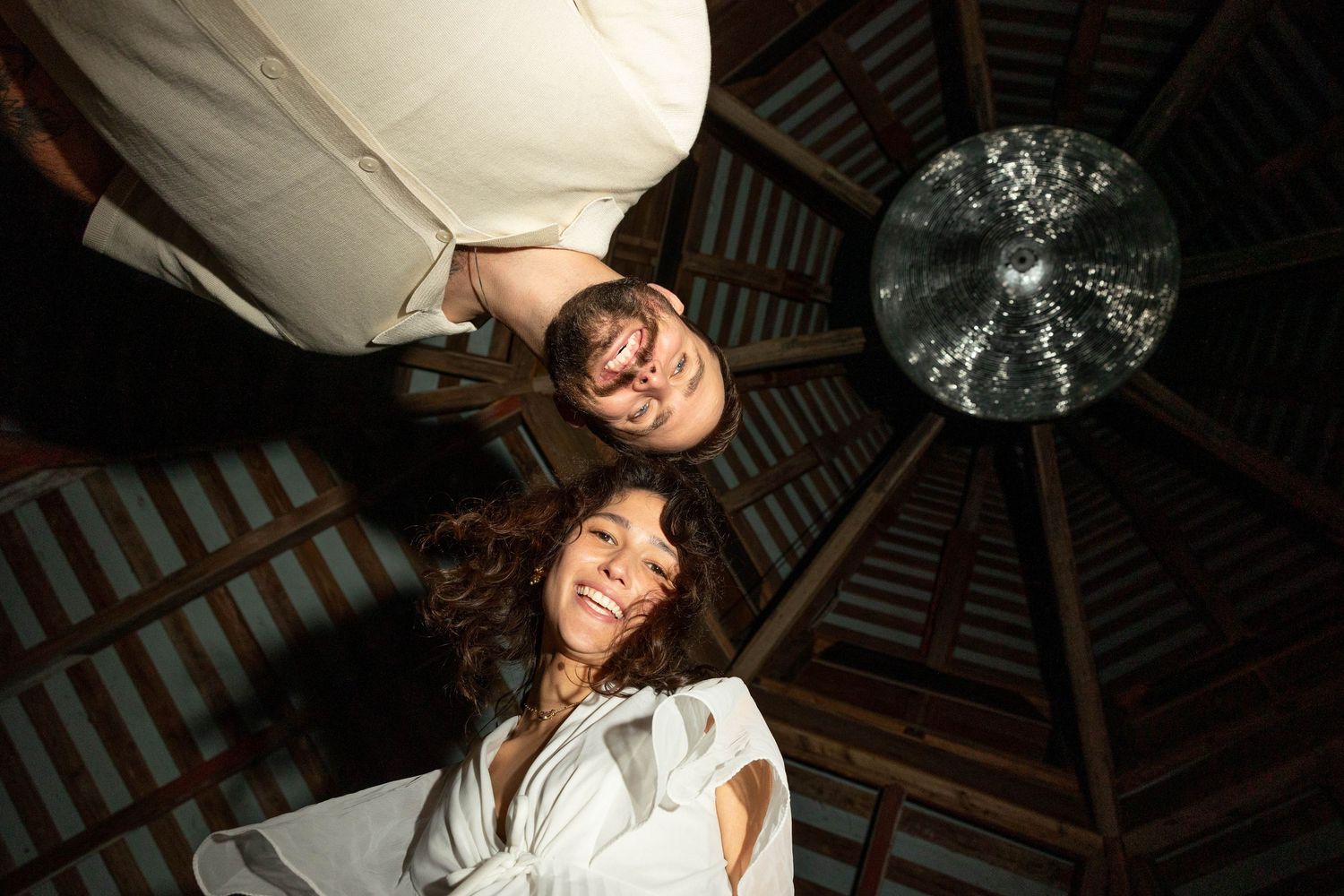 Low angle upward view of smiling couple beneath wooden gazebo ceiling with disco ball.
