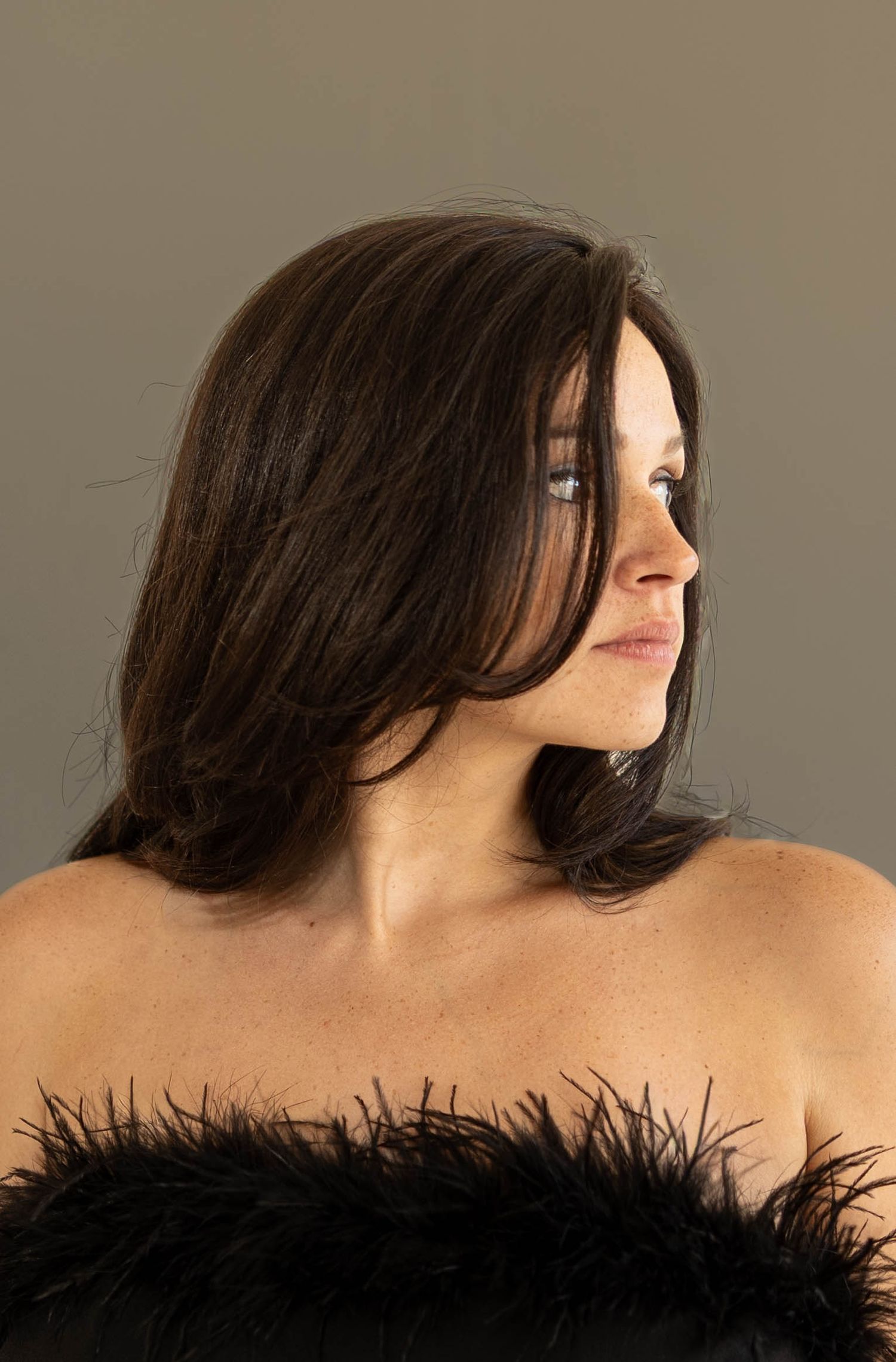 Woman with dark hair wearing a black feather strapless top, photographed in side profile.