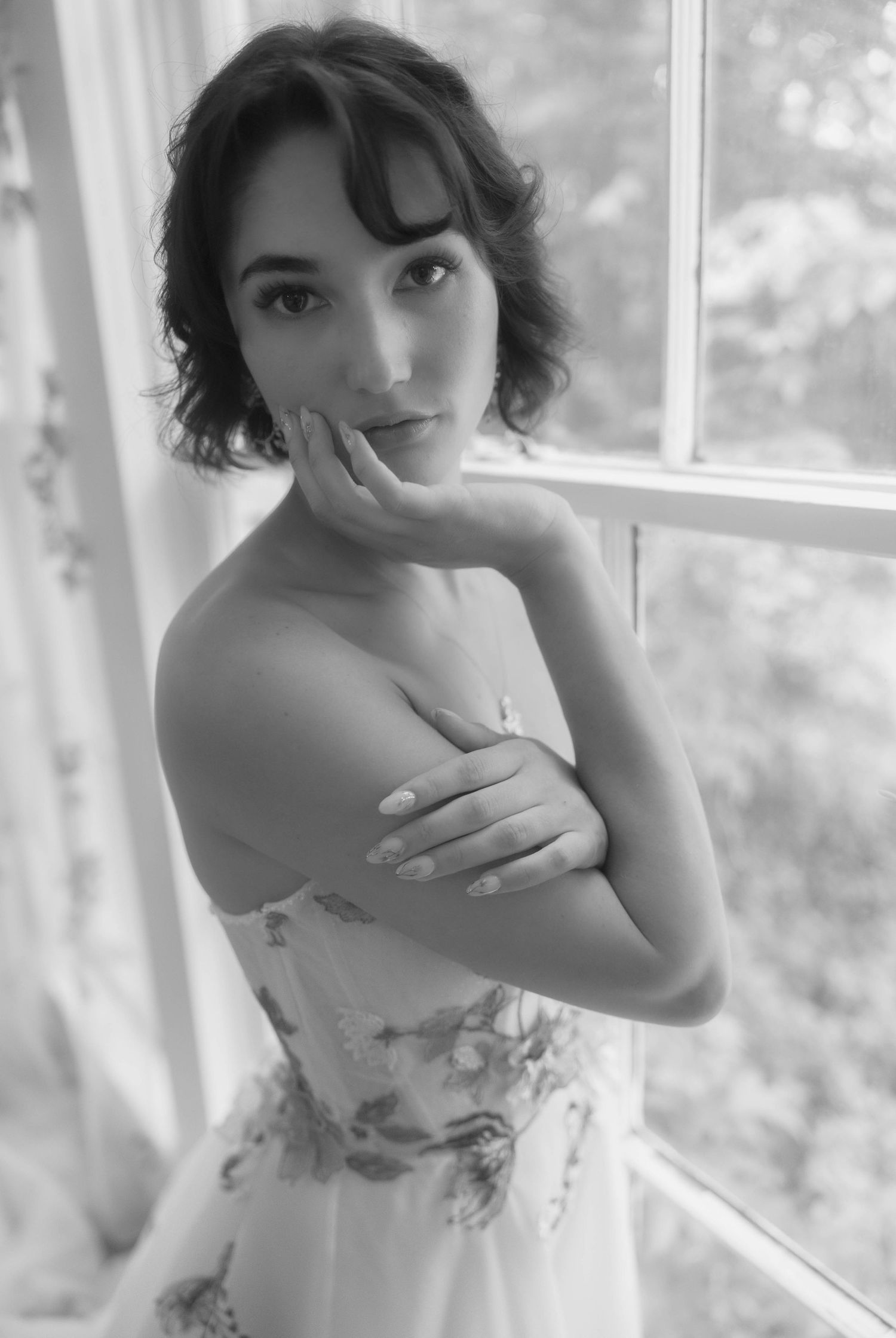 Black and white portrait of a bride in a strapless gown posing by a window.