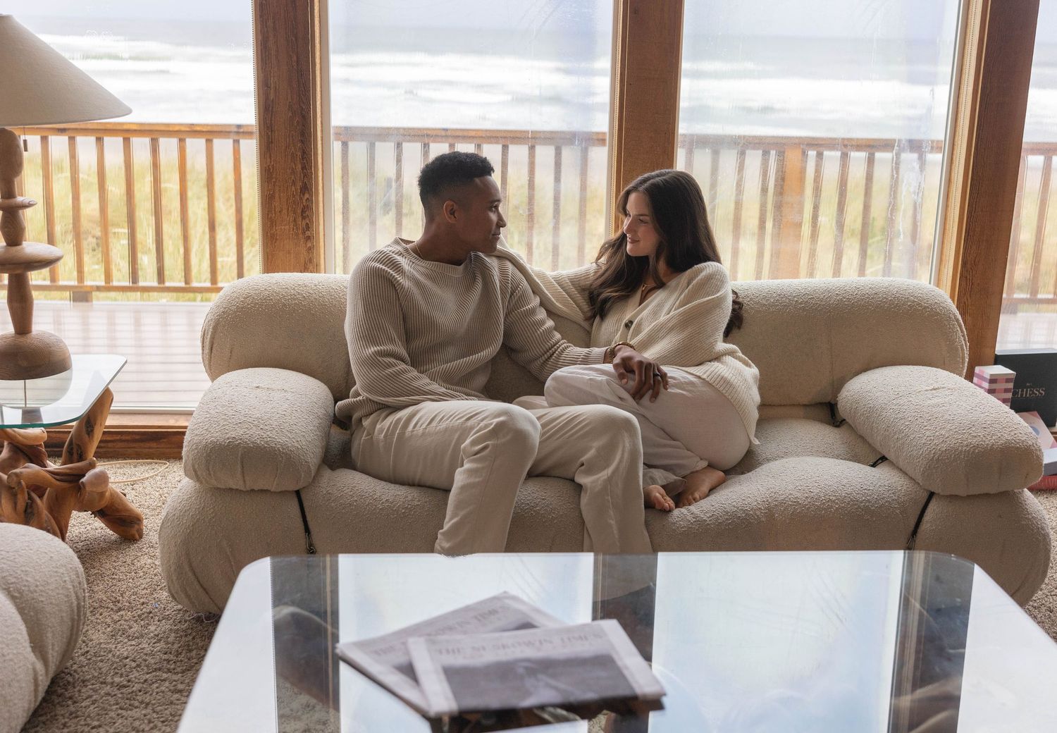 People relaxing on a comfortable white sofa in a bright, modern living room with large windows.