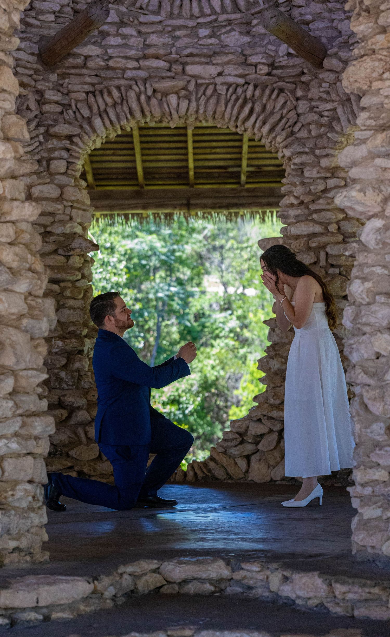 Two people sit in stone archways at a historic site with natural light filtering through green bamboo shades.