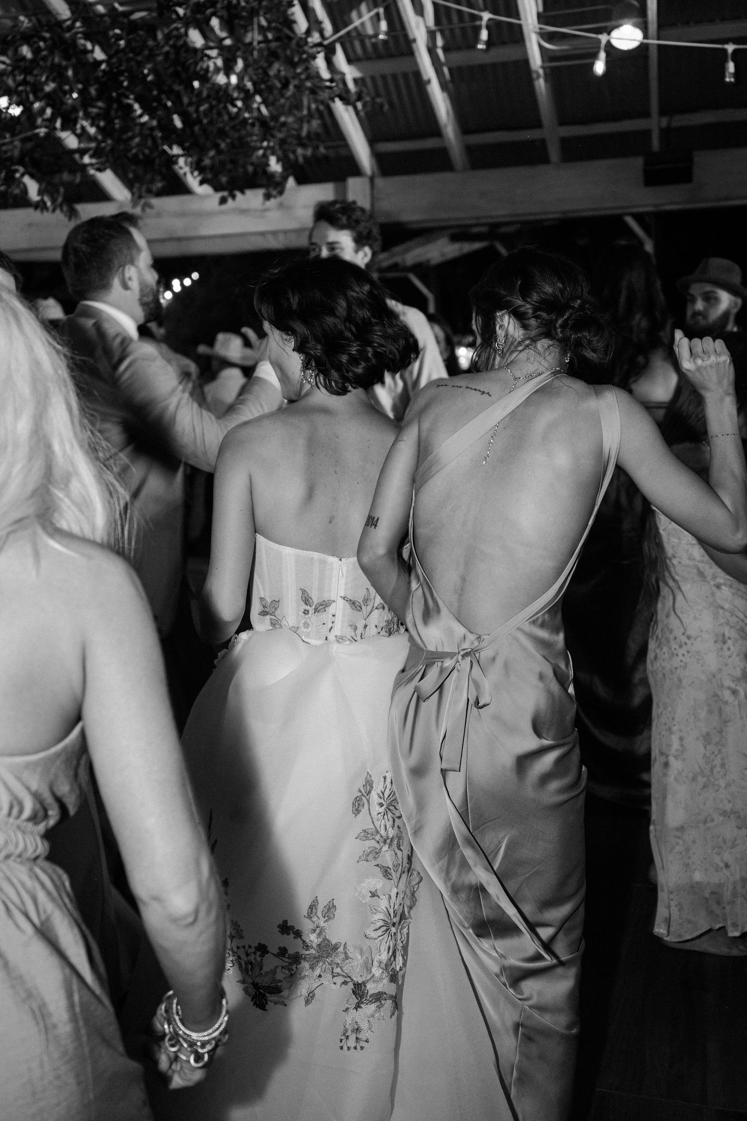 Black and white photo of wedding guests dancing at a reception under string lights.