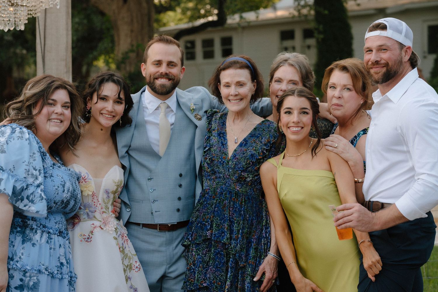 Group of smiling wedding guests posing together outdoors at a garden wedding celebration.