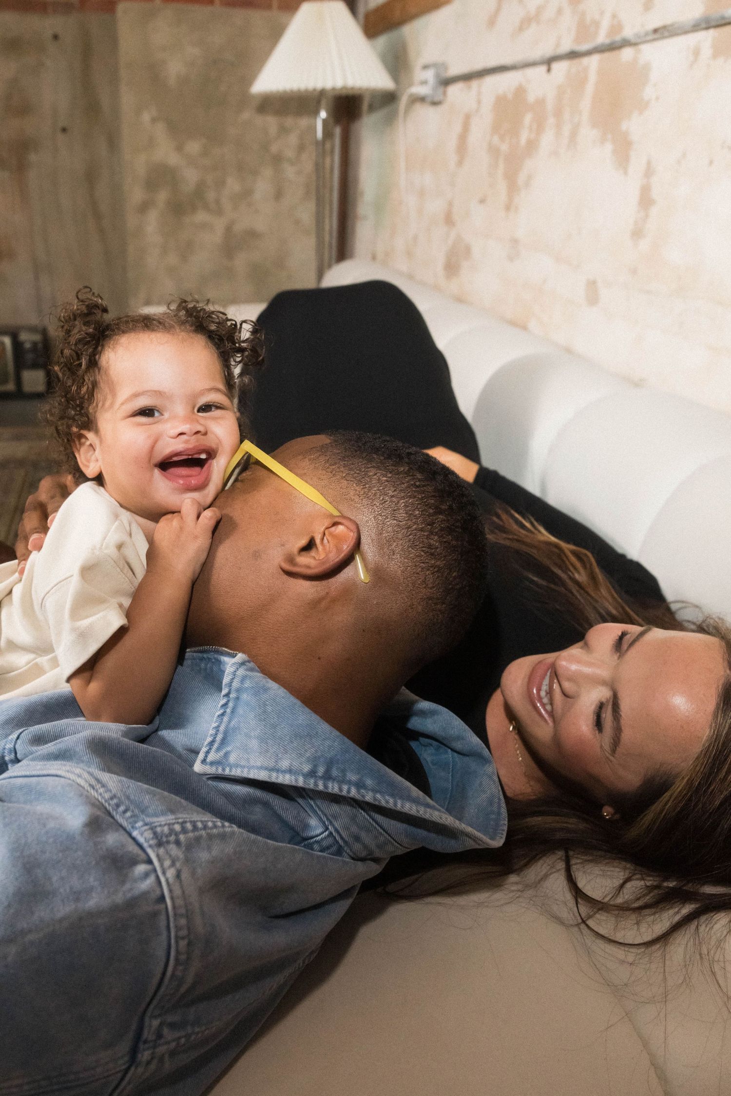 A joyful family moment with a laughing toddler, a man in denim, and a woman relaxing on a sofa.