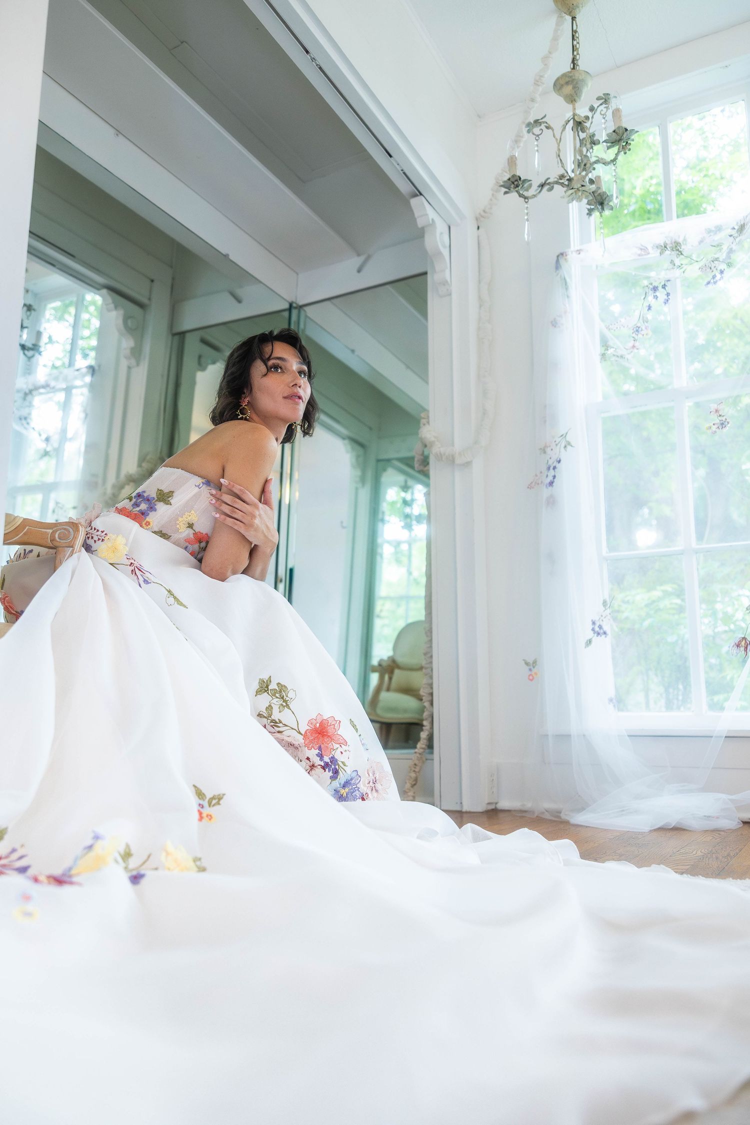 Bride in voluminous floral embroidered gown seated in bright sunlit vintage room.

Bridal portraits