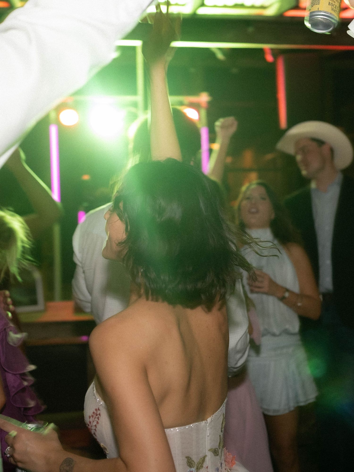 Guests dance energetically under colorful neon lights at a lively wedding reception party.