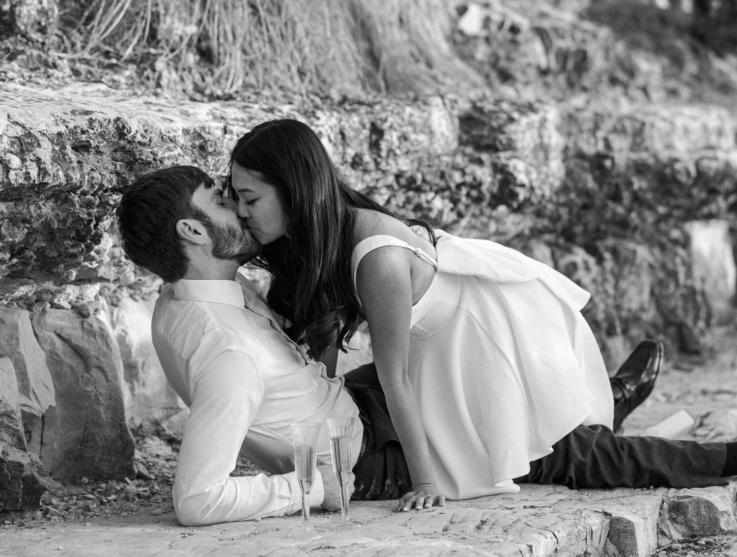 Black and white romantic photo of a couple kissing on rocky ground outdoors.