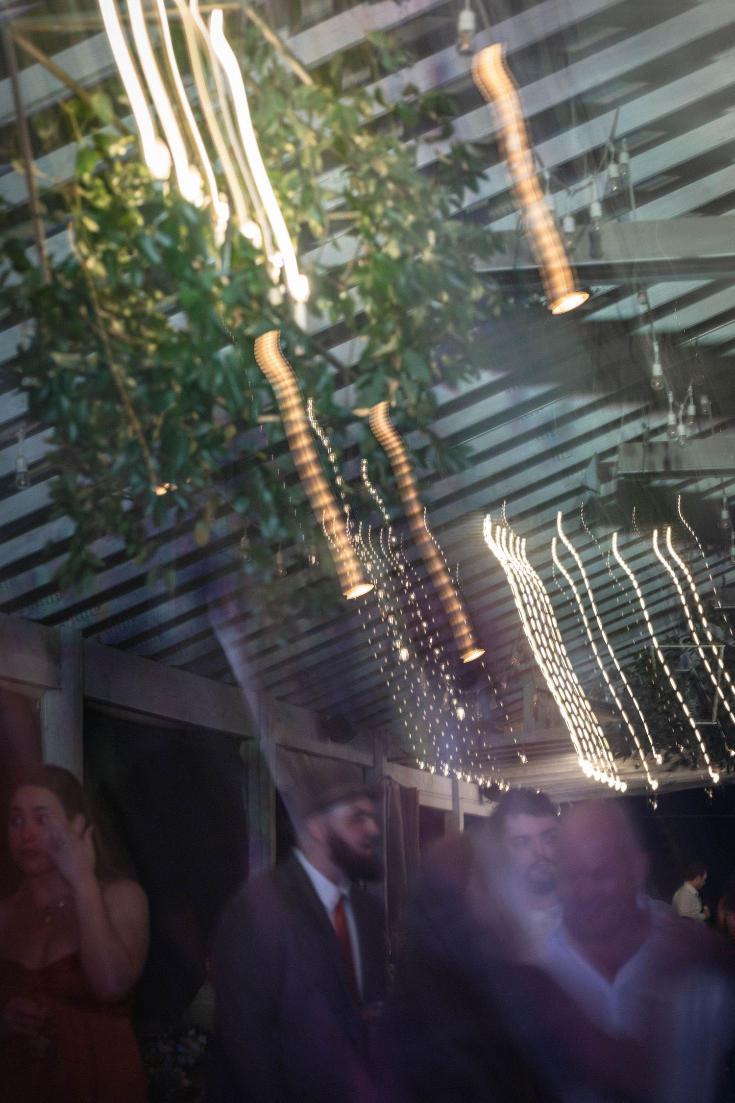 Elegant wedding reception venue with string lights and hanging pendants illuminating guests dancing below lush greenery.