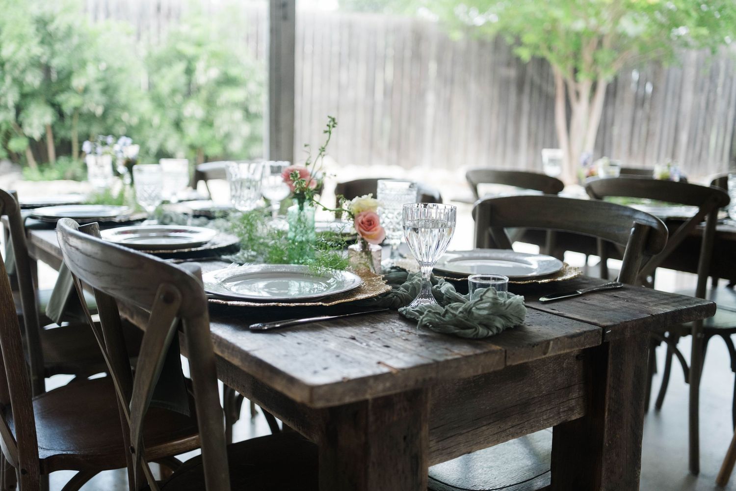 Rustic wooden farm table elegantly set with floral centerpieces and glassware for a wedding reception.