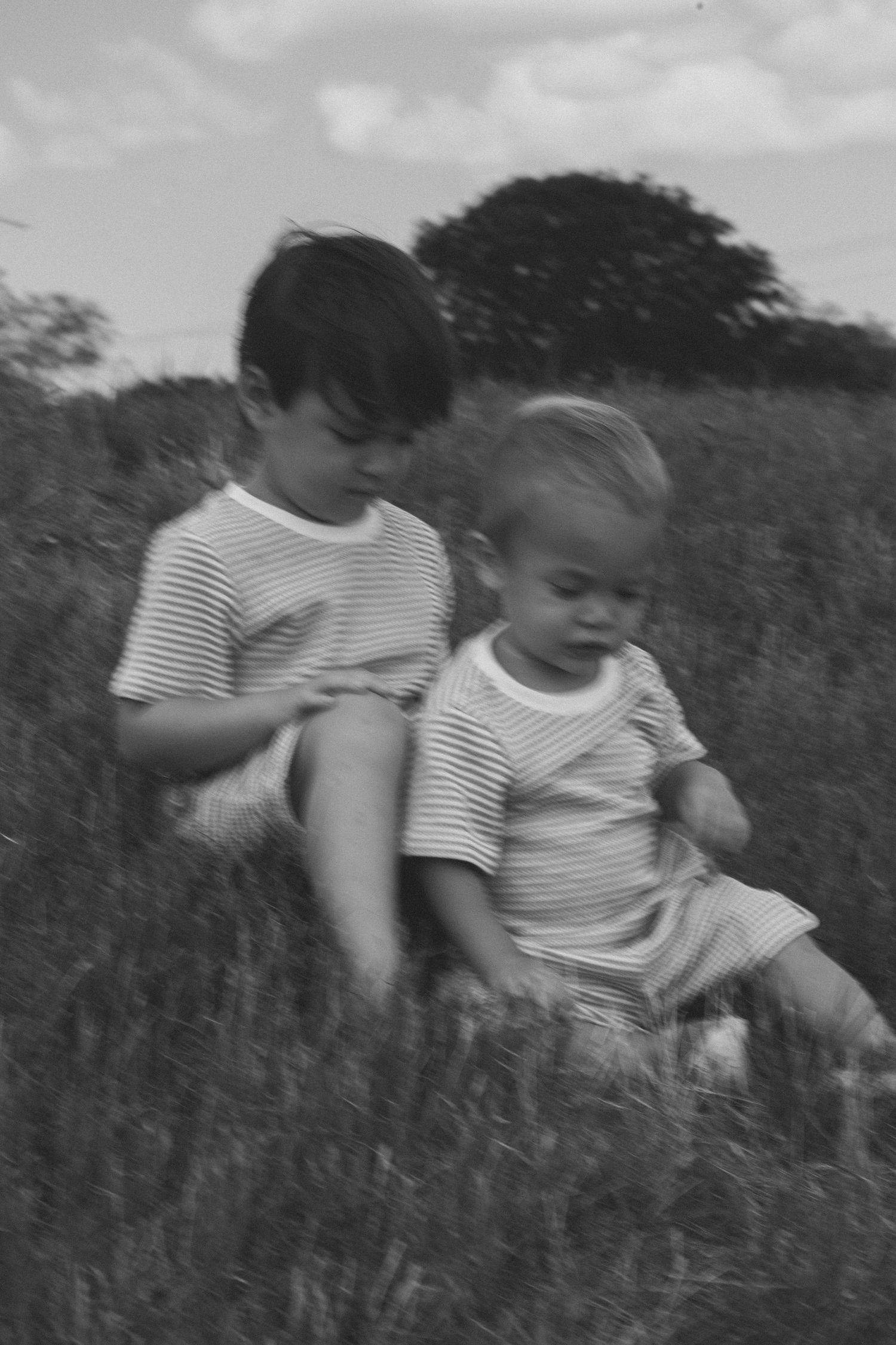 Two young children in matching striped shirts sitting together in grassy field in black and white.