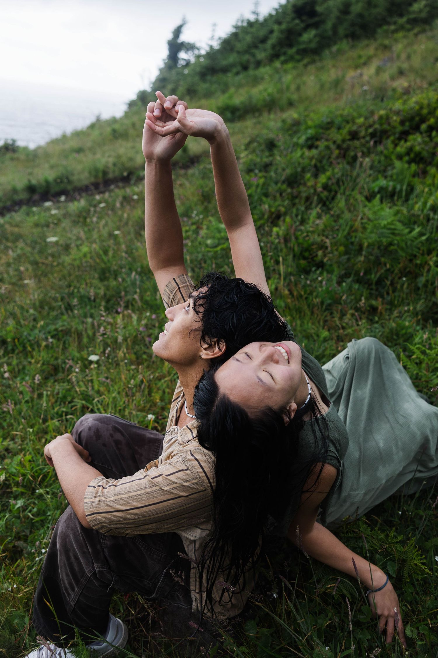 Couple holding hands while lying on lush green hillside grass in casual outdoor photography session.