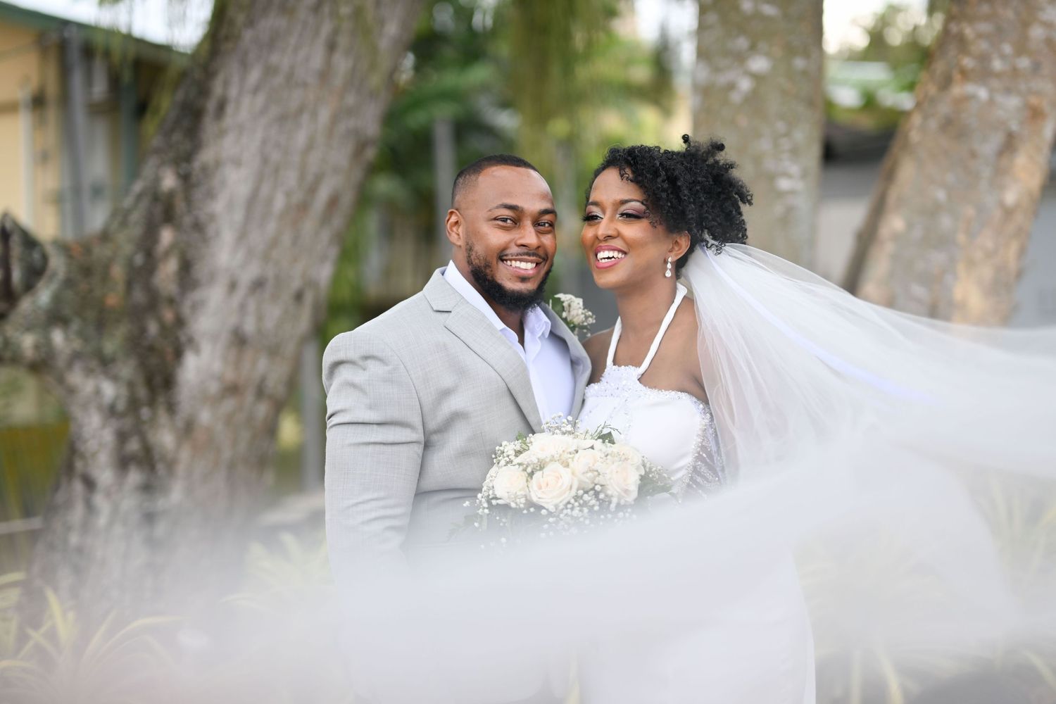 Happy newlyweds sharing a joyful moment together in their wedding attire under trees.