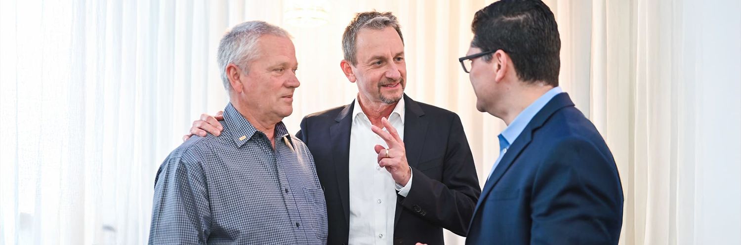 Three people engaged in a business discussion while standing in a bright office setting.