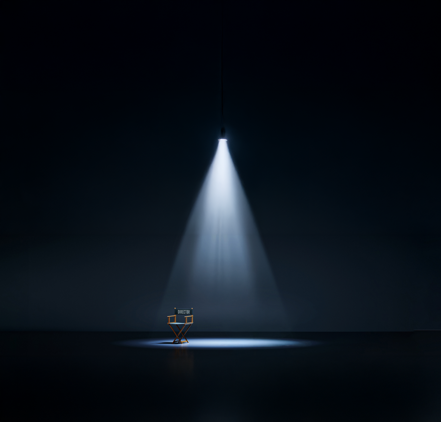 Dramatic overhead spotlight beam illuminating a chair in dark atmospheric setting.
