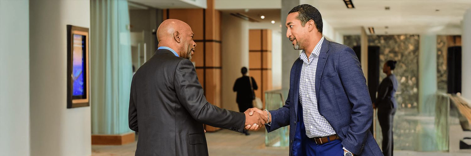 Two businessmen having a professional handshake greeting in a modern office hallway.