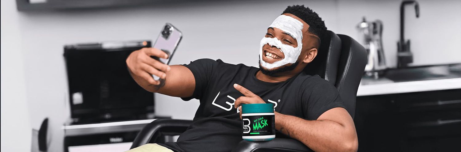A person wearing a black t-shirt smiles and takes a selfie while reclining in a modern kitchen setting.