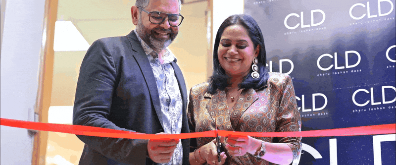 Two people smile while preparing to cut a red ribbon at a ceremonial opening event with CLD logos visible in background.