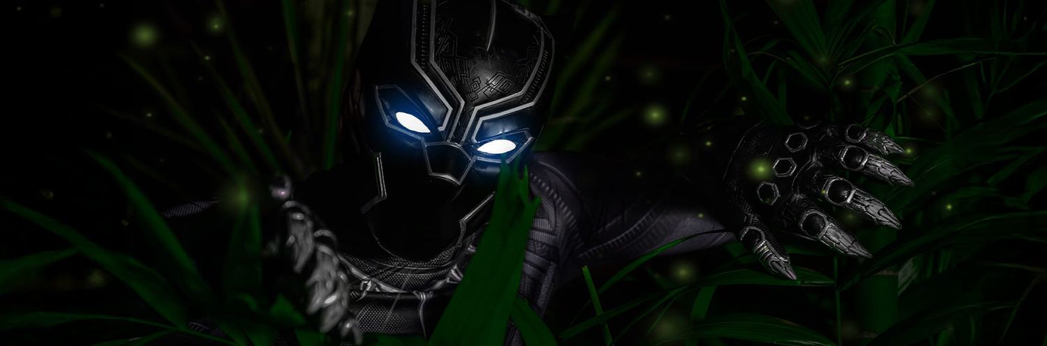 Glowing blue eyes illuminate through dark foliage in a menacing close-up of Black Panther's masked face.