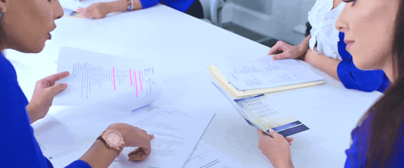 Team members in blue uniforms review documents and take notes during a business meeting at a table.
