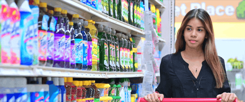 A person shops in a convenience store, standing beside shelves stocked with colorful beverage bottles.