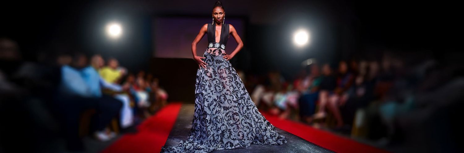 A model walks down an illuminated runway wearing a dramatic black and white voluminous ballgown during a fashion show.