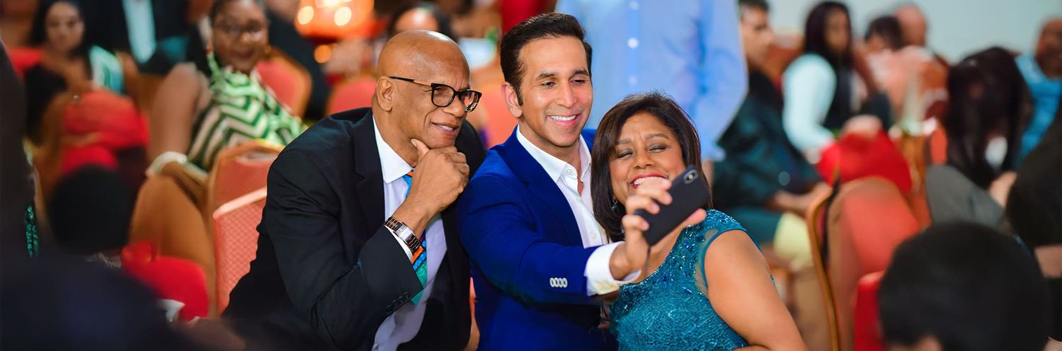 Three people share a joyful moment together at what appears to be a lively indoor event with a red backdrop.