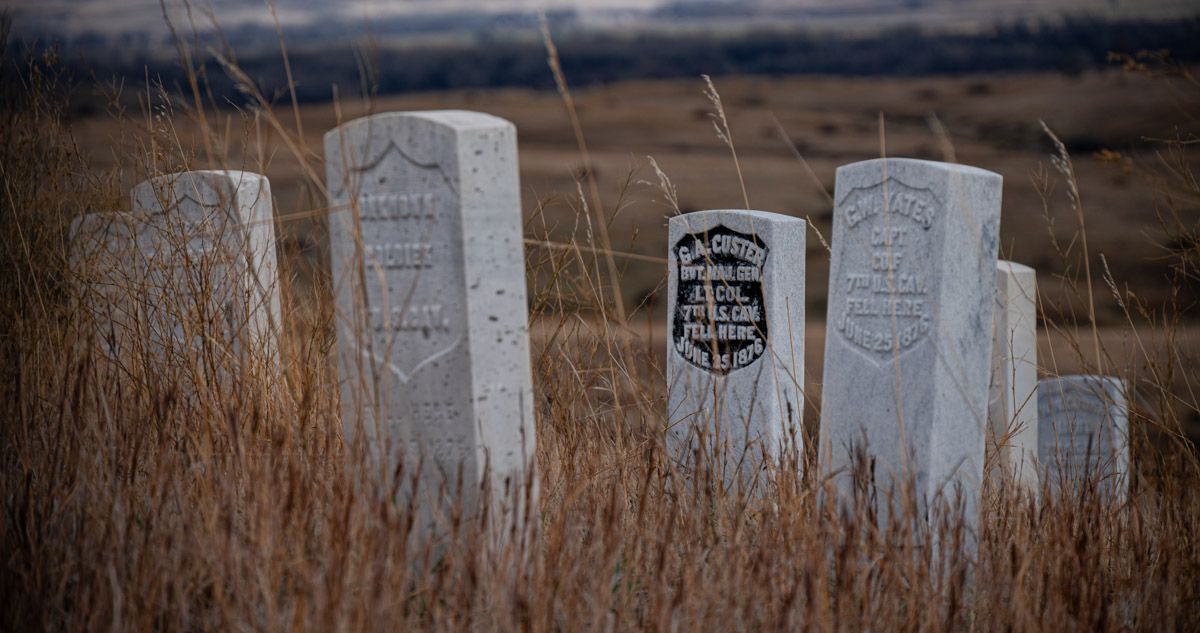 Weathered gravestones in an overgrown field under a cloudy sky. Image by Mark Swanson Photography.