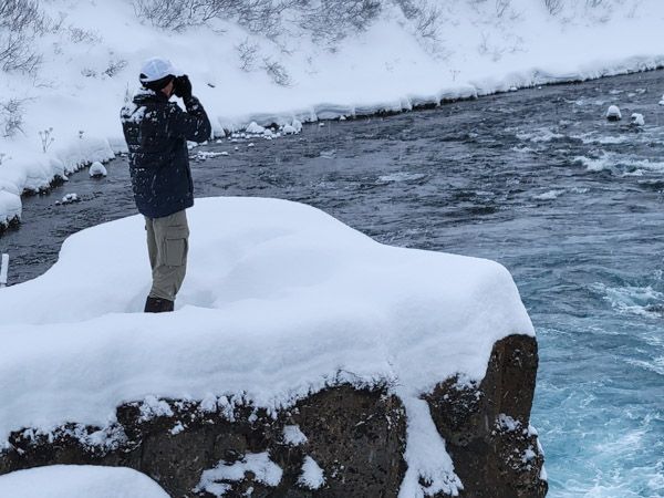 Photographer Mark Swanson standing atop a snowy cliff photographing icy water.