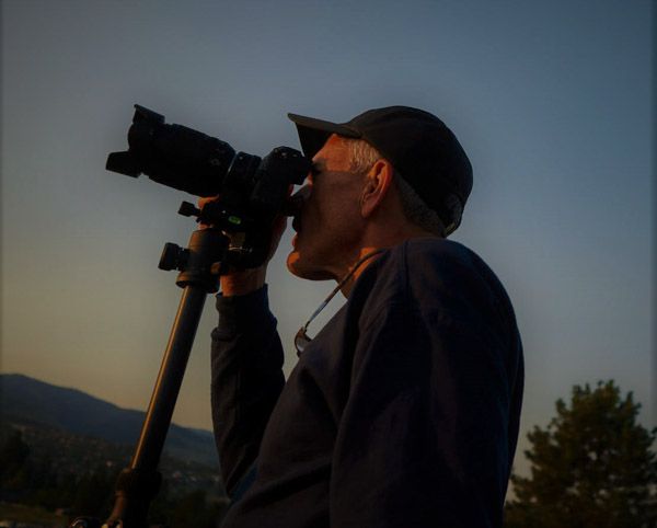 Photographer Mark Swanson using his camera against a sunset sky.