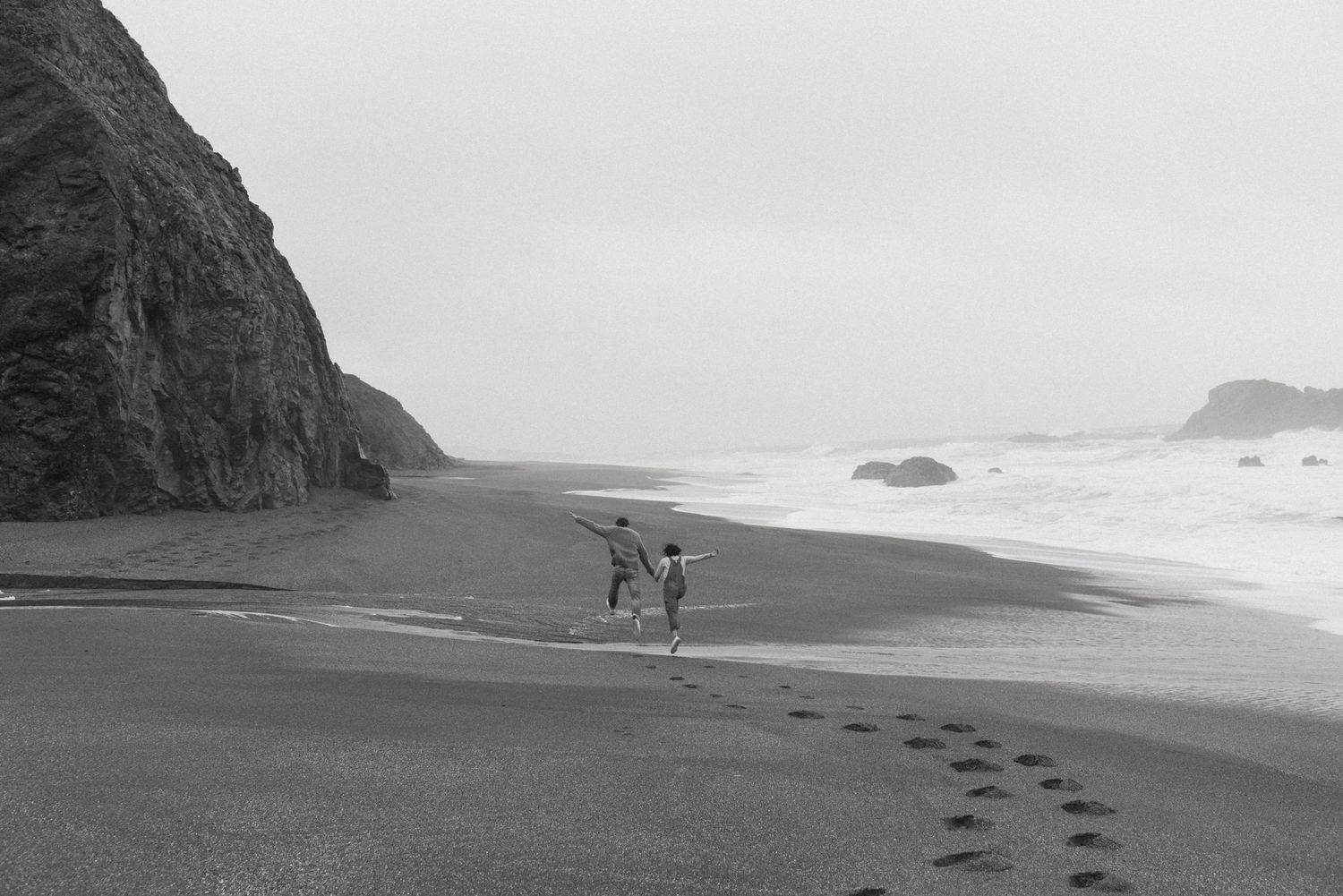 Couple running on the beach at their engagement session in Bodega Bay California