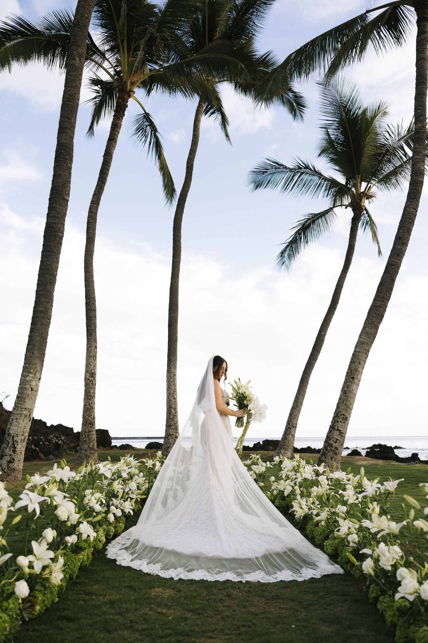 bride poses in custom wedding dress with flowers amidst palm trees in Maui, Hawaii