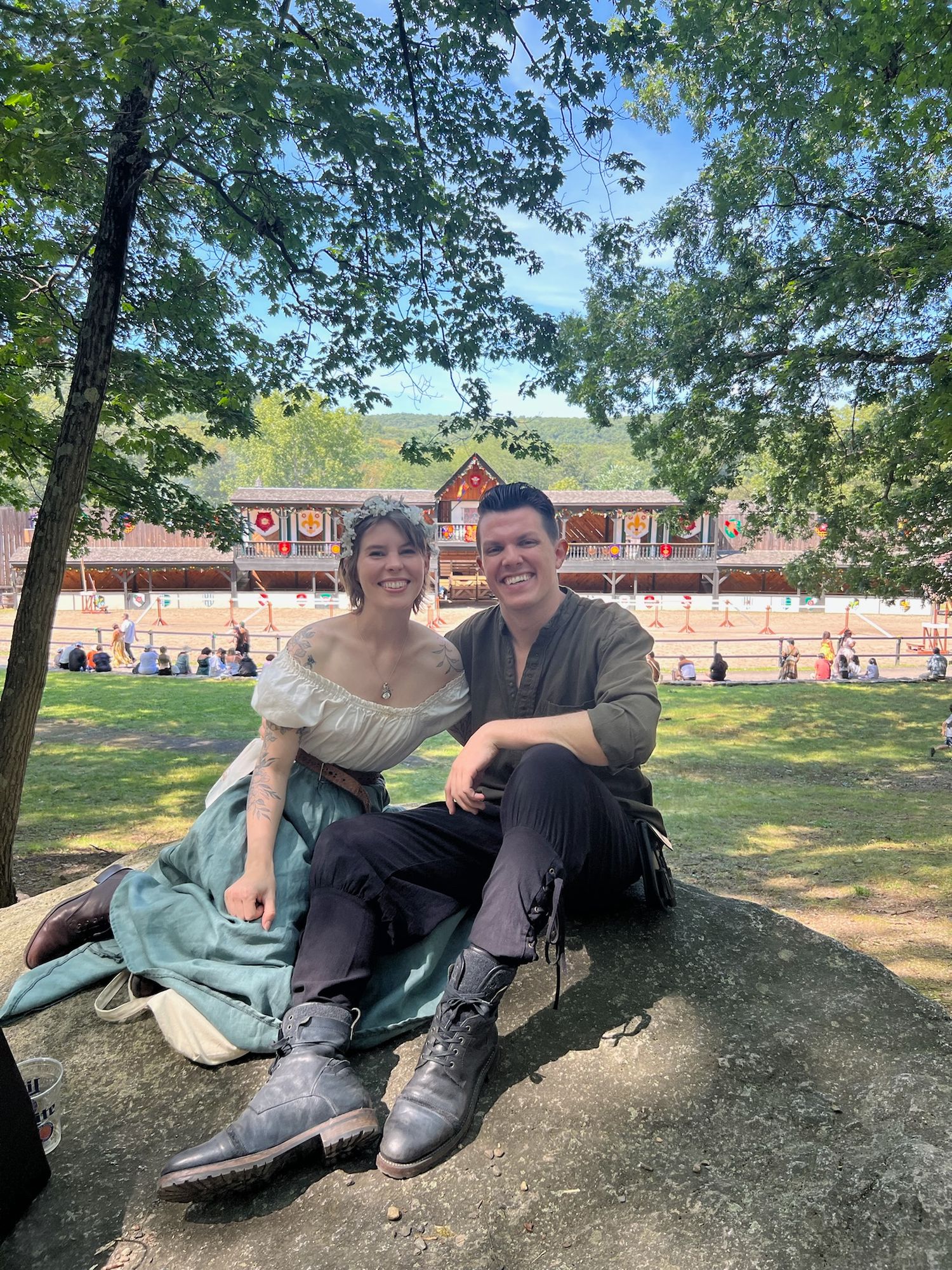 Couple sitting together on rock with rustic building in background.