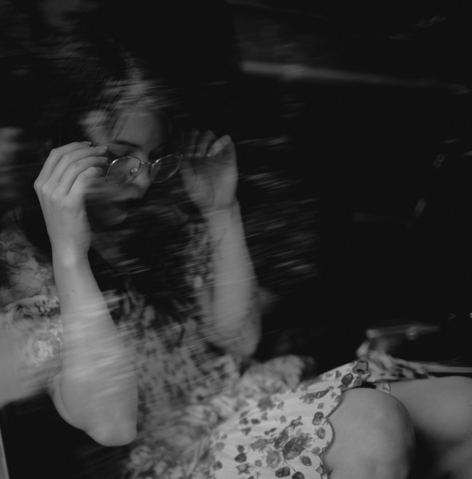 A blurry black and white photo showing raised hands against a floral print in a dark atmospheric setting.