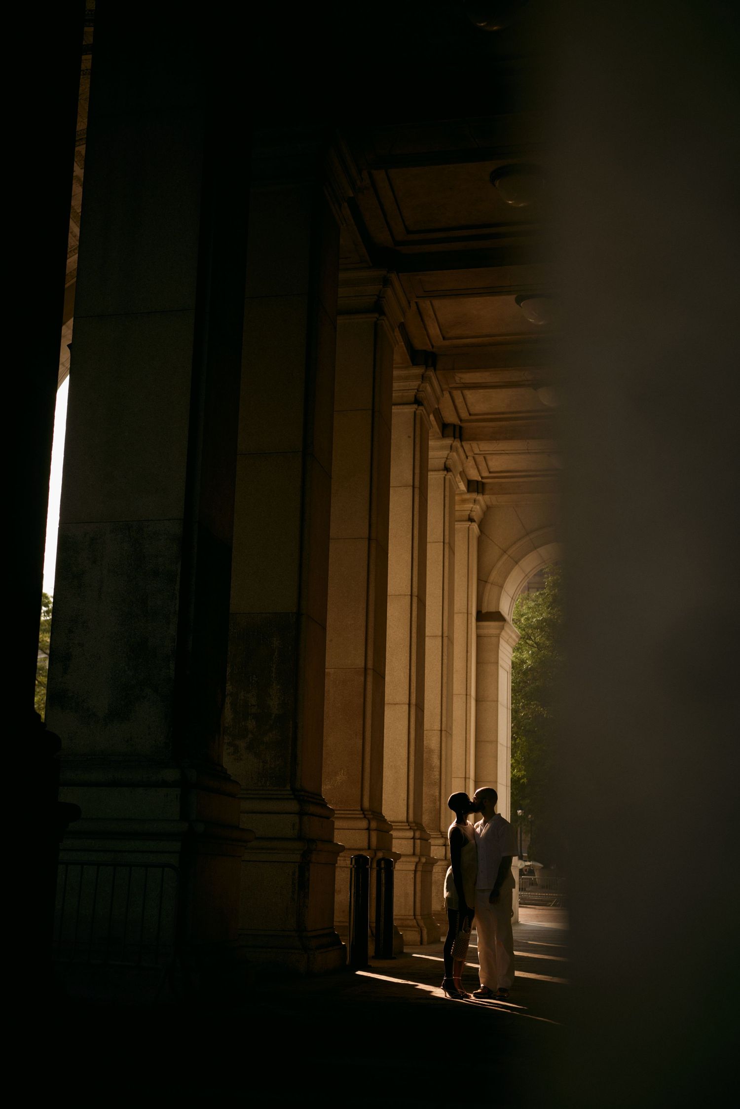 A silhouetted couple embracing in dramatic light beneath historic stone columns during New York City Hall Elopement session.