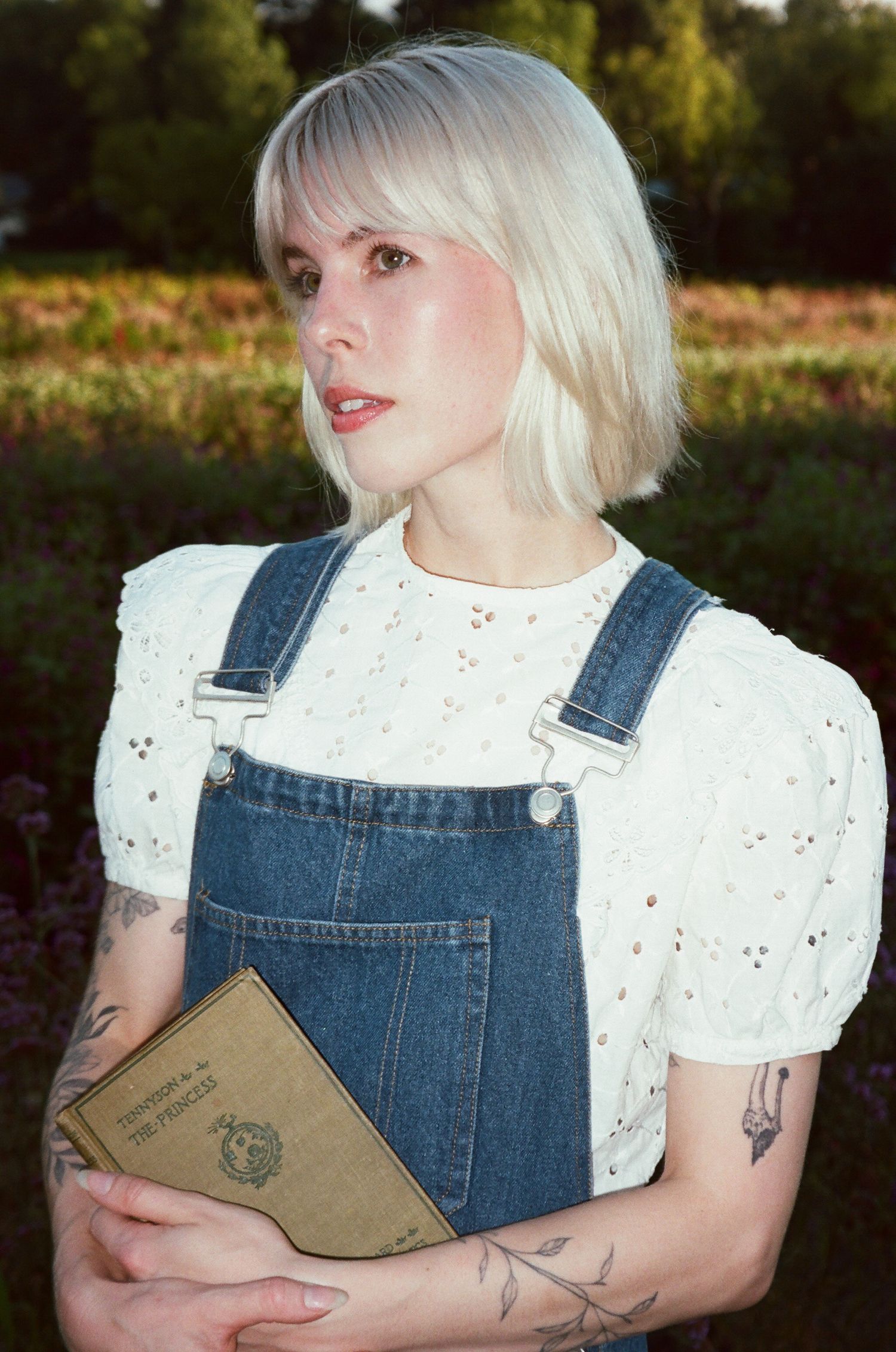 A vintage-style portrait of a girl in denim overalls and white blouse holding an old book.